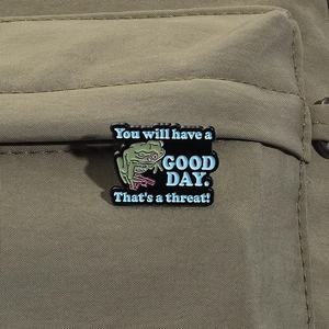 Detail of green frog enamel pin with a pink gun on an olive green canvas backpack