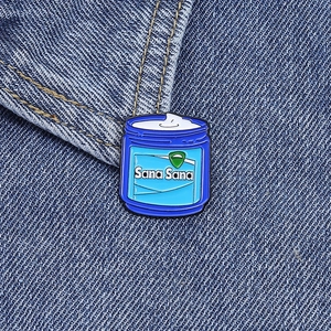 Close-up of Sana Sana enamel pin with a smiling jar design on blue denim jacket