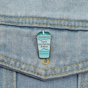 Enamel beverage cup pin with 'A blast' text pinned on a blue denim jacket