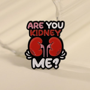 Detail of red kidney enamel pin with funny 'ARE YOU KIDNEY ME?' pun text on metal