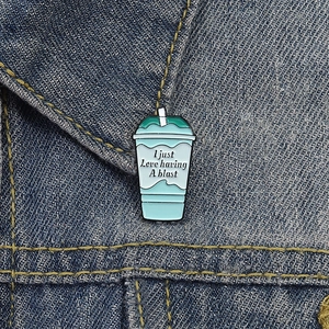 Detail of teal enamel baja blast pin on denim jacket with I just love having a blast text