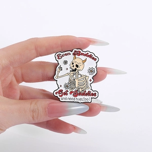 Detail of skull enamel pin with Even Baddies Get Saddies slogan held by hand
