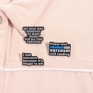 Detail von drei schwarzen Sarkasmus-Emaille-Pins an einem rosa Jeansjackenkragen