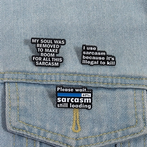 Detailansicht von drei Emaille-Pins mit Sarkasmus-Zitaten an einer blauen Jeansjacke