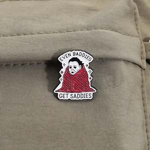 Detail of Michael Myers enamel pin with Even Baddies Get Saddies text on canvas