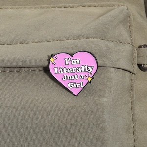 Detalle macro del broche de corazón rosa con frase I'm Literally Just a Girl sobre mochila