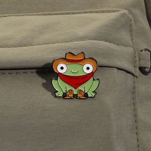 Detail einer kreativen Cowboy-Frosch-Emaille-Anstecknadel auf einem grünen Rucksack