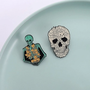 Detail of two unique Halloween enamel pins featuring cute cats in skull shapes on a tray