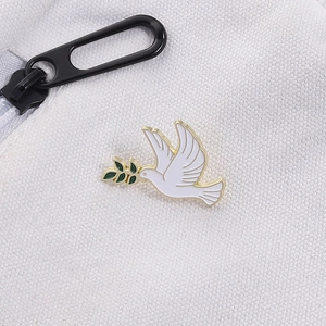 Close-up of white dove enamel pin with green olive branch and golden metal edges
