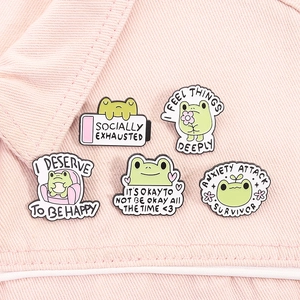 Detail showing high-quality enamel frog pins set with cute quotes on pink fabric background
