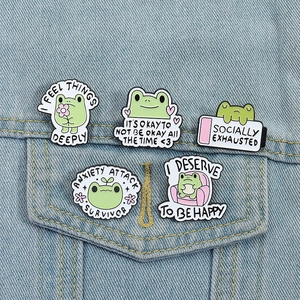Close-up of five cute green frog enamel pins on a light blue denim jacket pocket