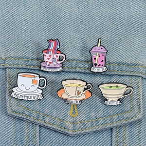 Detail of five cute enamel pins with tea puns pinned on a blue denim jacket pocket