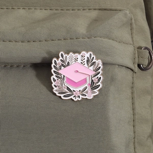 Pink graduation cap enamel pin with golden outlines on green canvas bag background