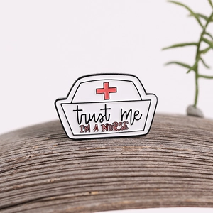 Nurse hat enamel pin with Trust Me I'm a Nurse text and red cross on wood background