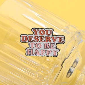 Vista macro della spilla smaltata YOU DESERVE TO BE HAPPY con design colorato vivace
