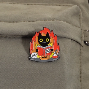 Detail einer Emaille-Anstecknadel mit schwarzer Katze und Feuer auf einer grünen Tasche