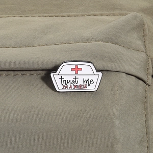 Detailed enamel nurse hat pin with trust me text pinned on a canvas backpack surface