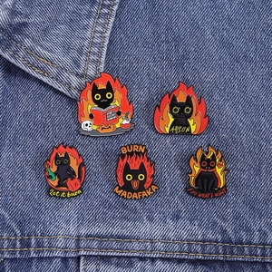 Detail of five black cat enamel pins with orange flame motifs on a denim jacket