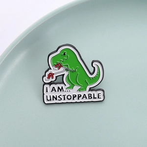 Macro shot of green dinosaur enamel pin featuring 'I AM... UNSTOPPABLE' text design