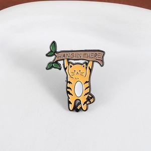 Détail d'un pin's en émail avec chat suspendu à une branche et texte Hang In There