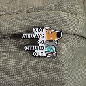 Spilla smaltata cane cartoon con testo 'Not Always So Chilled Out' su sfondo verde