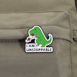 Detail of green T-Rex enamel pin with I Am Unstoppable text on green fabric