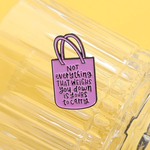 Dettaglio di spilla a borsa in smalto rosa con scritte motivazionali su vetro