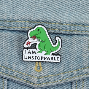 Detail of green T-Rex enamel pin with 'I AM UNSTOPPABLE' text on blue denim jacket