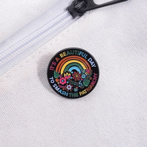 Detail of round enamel brooch with rainbow, flowers, and social slogan on white bag