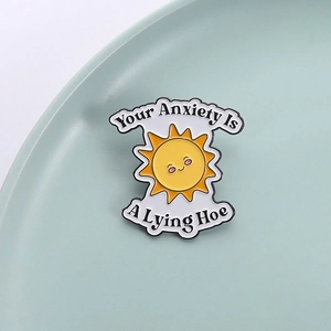 Pin's émaillé tournesol avec citation humoristique posé sur un plateau en céramique bleu