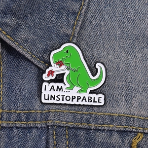 Funny green dinosaur enamel pin with I Am Unstoppable quote on blue denim jacket