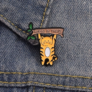 Detail der orangefarbenen Emaille-Anstecknadel mit Katze und Spruch auf Denim