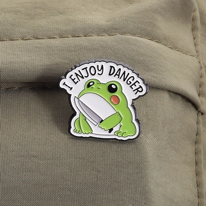Detailed macro view of a green frog enamel pin with a knife on a canvas backpack