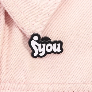 Makroaufnahme einer Emaille-Brosche mit YOU-Text auf rosa Denim-Stoffhintergrund