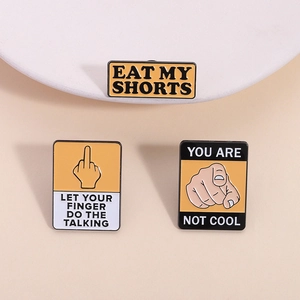 Three yellow enamel pins with bold typography and funny hand gestures on a minimalist base