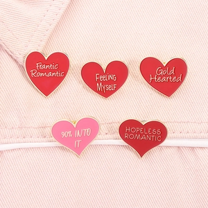 Dettaglio di spille smaltate a cuore con testo romantico su sfondo denim rosa