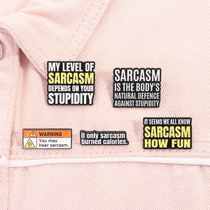 Detail of five enamel sarcasm pins with funny quotes on a light pink denim jacket