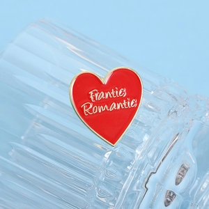 Dettaglio di una spilla a cuore smaltata rossa con scritta Frantic Romantic