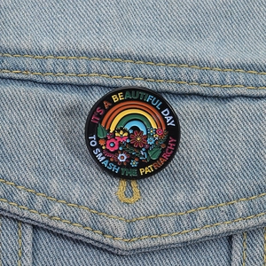 Detail of round enamel rainbow flower brooch on a denim jacket with empowering text