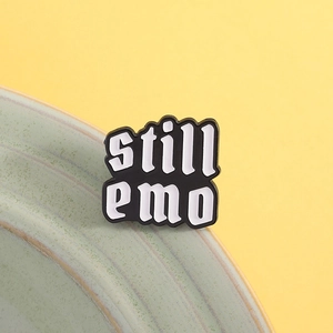 Detail shot of the Still Emo enamel pin featuring black and white lettering on a ceramic plate