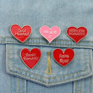 Set di cinque spille smaltate a cuore rosso con frasi romantiche su giacca di jeans