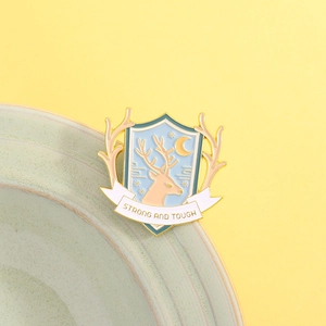 Detail of shield-shaped enamel pin with deer, stars and Strong and Tough inscription