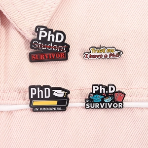 Détail de quatre broches émaillées de doctorat avec toque sur un tissu en denim rose pâle