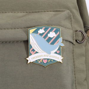 Macro view of blue whale enamel pin with Freedom and Wisdom text on green canvas