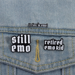 Close-up of Emo-themed enamel pins featuring still emo text on a blue denim jacket