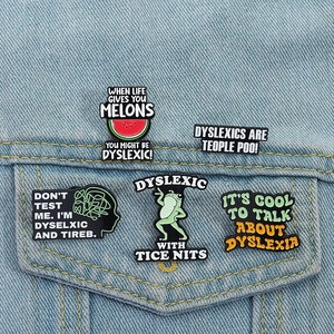 Détails de cinq pin's en émail pour la dyslexie sur une poche de veste en jean bleu clair
