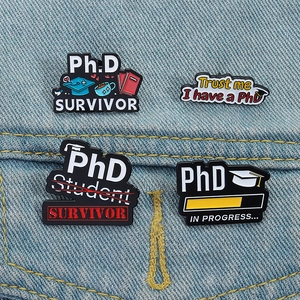 Détail de quatre épinglettes en émail PhD avec humour sur tissu denim bleu