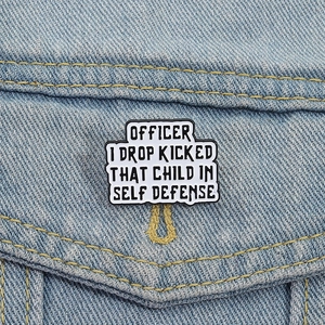 Detail of cartoon enamel pin with humor quote on blue denim jacket pocket