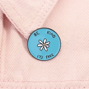 Makroaufnahme der blauen Emaille-Brosche mit Gänseblümchen-Motiv auf rosa Denim-Stoff