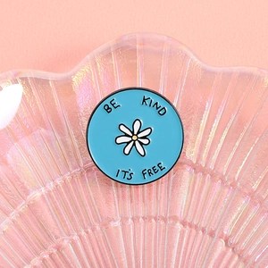 Detailansicht der Emaille-Gänseblümchen-Brosche mit BE KIND Text auf einer Schale